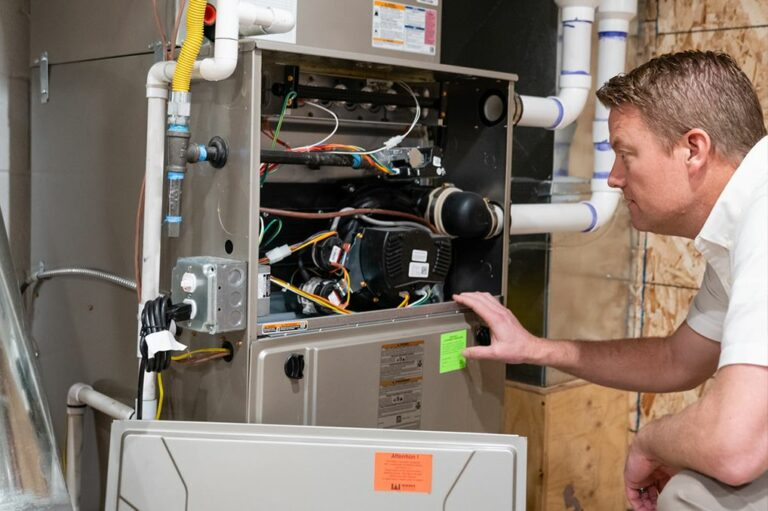 This image depicts a man, likely an HVAC technician, inspecting the open cabinet of a residential gas furnace.